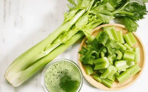 Jus de céleri frais, coupé en morceaux dans un bol en bois. Une branche entière de céleri est à côté. Attention à l'allergie céleri.