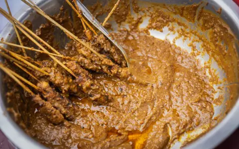 Brochettes de poulet baignant dans une généreuse sauce satay crémeuse, prêtes à être dégustées.