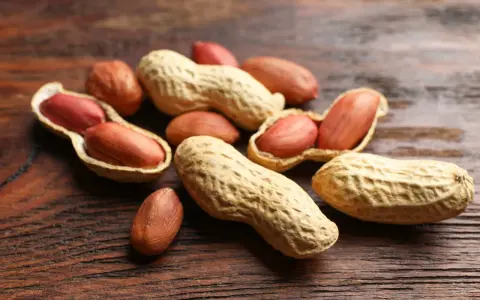 Un tas de noisettes arachides, certaines ouvertes révélant leurs grains rouges, sur un fond de bois sombre.