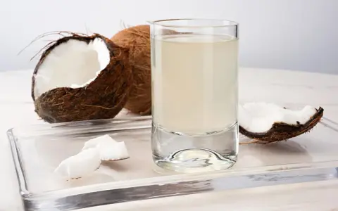 Un verre d'eau de coco, entouré de morceaux de noix de coco fraîches. Découvrez les nombreux bienfaits de l'eau de coco pour votre santé.