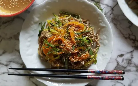Salade de nouilles soba colorée avec des carottes, des courgettes et des graines de sésame, servie avec une sauce crémeuse.