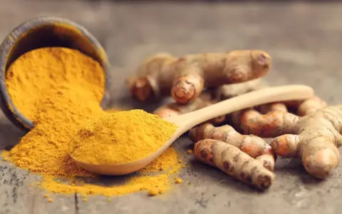 Racines de curcuma et poudre dorée sur une cuillère en bois, symbolisant le curcuma bienfait pour la santé.