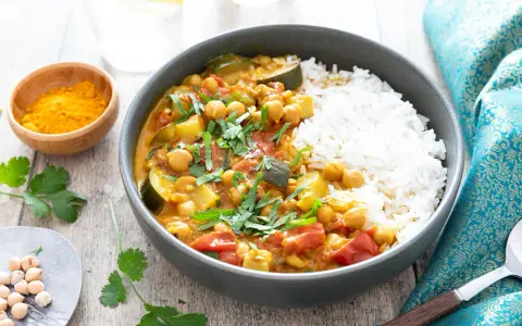 Un délicieux curry végétarien aux pois chiches, courgettes et tomates, servi avec du riz blanc et garni de coriandre fraîche.