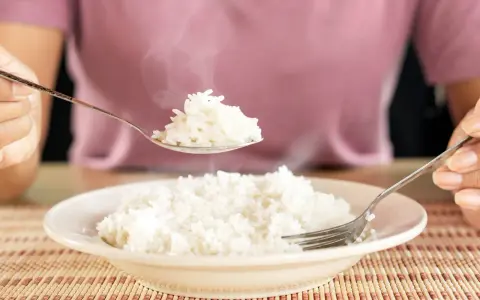 Une cuillère de riz blanc fumant, résultat d'une cuisson parfaite, est soulevée au-dessus d'une assiette remplie.