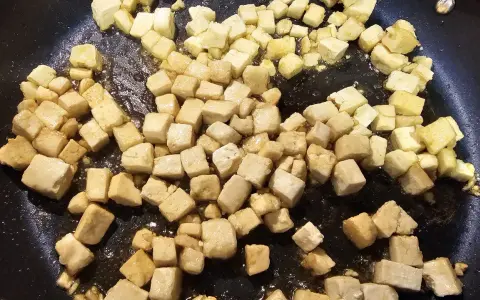 Dés cubes de tofu caramélisé dorent dans une poêle, prêts à être dégustés.