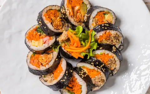 Un assortiment de makis végétariens colorés, garnis de carottes râpées, d'omelette et de légumes croquants, disposés en cercle sur une assiette blanche.