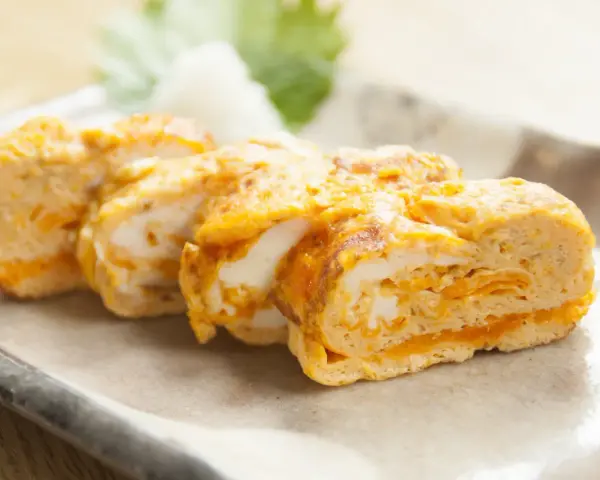 Délicieux oeuf japonais roulé, aux couches dorées et blanches, servi sur une assiette avec une feuille verte.