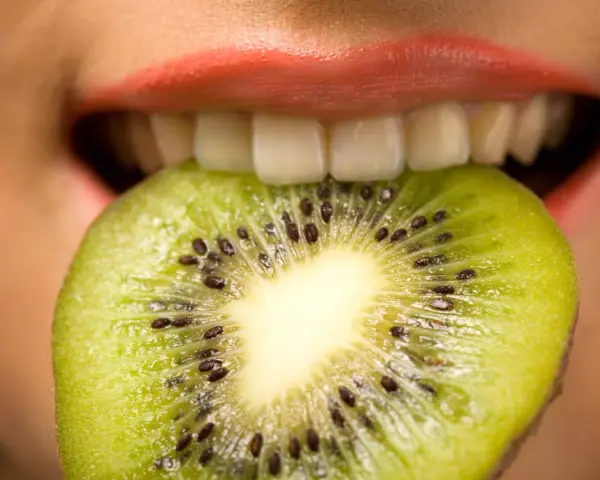 Une tranche de kiwi est mordue par des lèvres roses, ses petites graines noires contrastant avec la chair verte. Une sensation de kiwi langue qui pique.