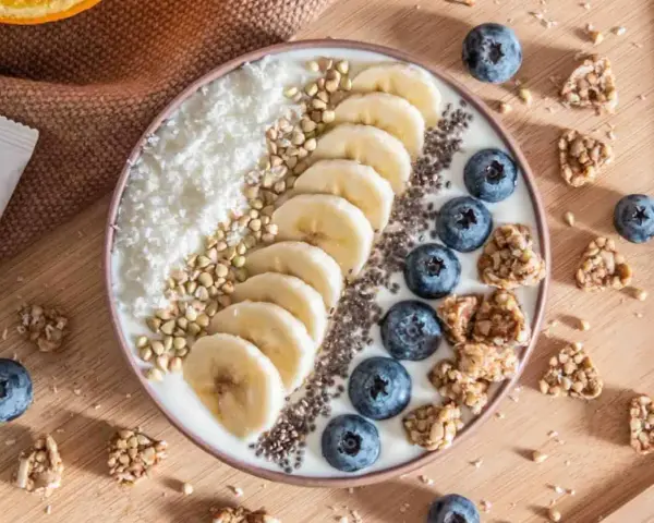 Un bol de smoothie aux bananes, myrtilles, noix de coco râpée et graines de chia, parfait pour un déjeuner au bureau sain et gourmand.