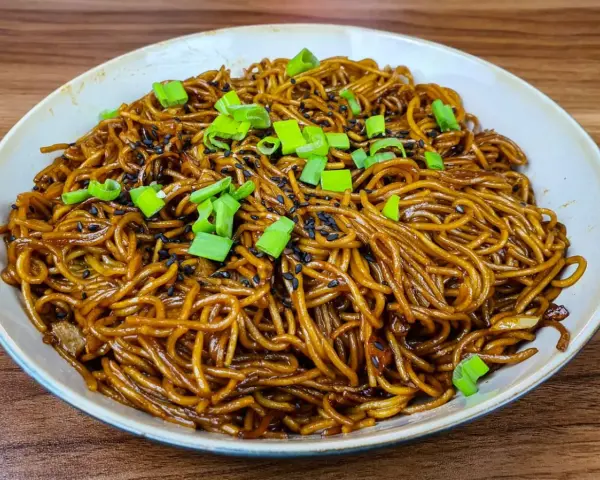 Un plat de nouilles savoureuses, enrobées d'une sauce brune appétissante, garnies de graines de sésame noir et de ciboule fraîche.