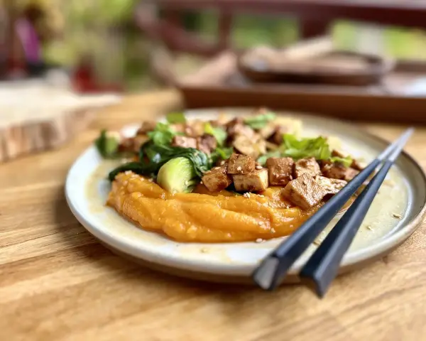 Un plat savoureux de tofu miso sur une purée de patates douces, garni de légumes verts et de graines de sésame.