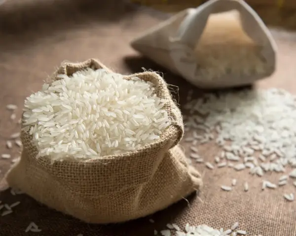 Un sac en toile de jute déborde de riz blanc, une céréale essentielle. Une autre bourse de riz est visible en arrière-plan.