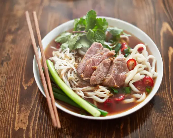 Un bol de soupe nouille de riz avec du bœuf, des germes de soja, des oignons verts et du piment rouge, prêt à être dégusté avec des baguettes.