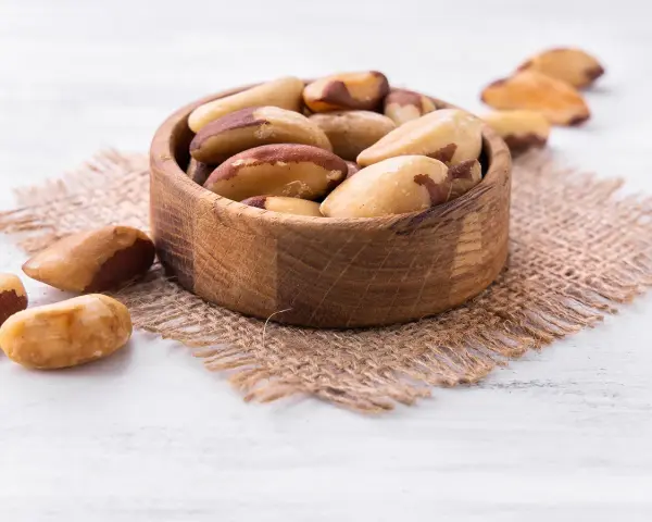 Un bol en bois rempli de noix du Brésil, mettant en avant leurs bienfaits nutritionnels. Quelques noix sont dispersées autour.