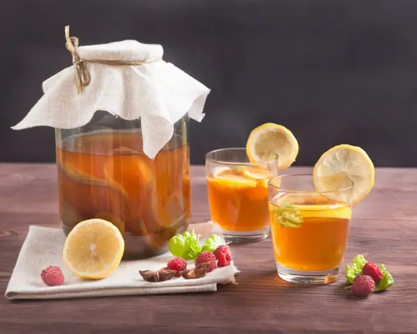 Bocal de kombucha et deux verres garnis de citron, framboises et menthe. Découvrez les kombucha bienfaits pour une boisson rafraîchissante et saine.