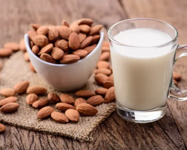 Un verre de lait d'amande frais à côté d'un bol d'amandes entières sur une surface en bois rustique.