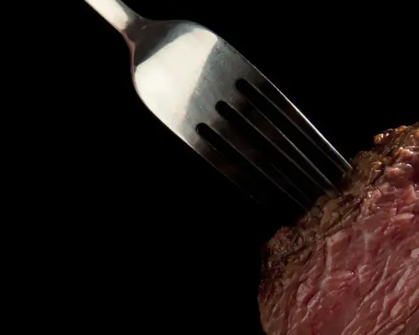 Une fourchette transperce un morceau de viande rouge, rappelant la prudence pour ceux qui ont une allergie au porc.