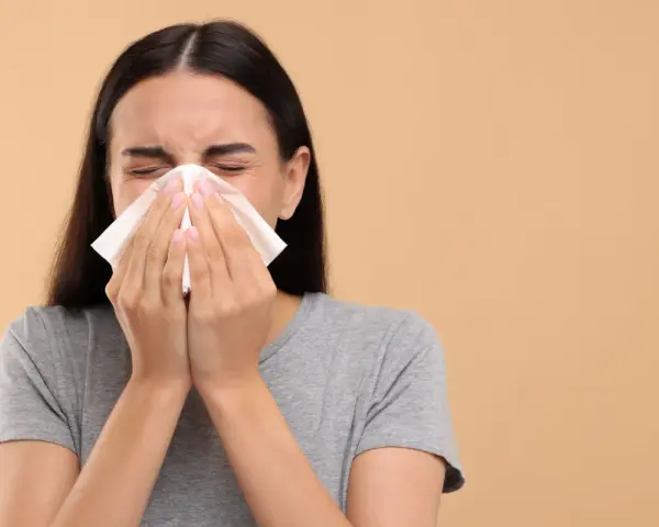 Une jeune femme se mouche dans un mouchoir en papier, le nez bouché par un rhume.