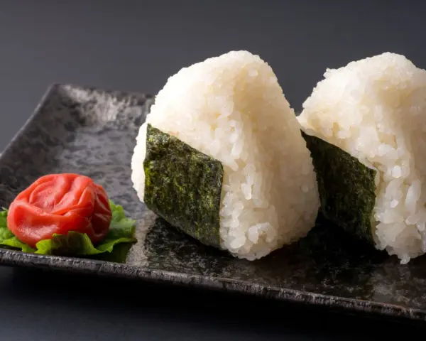 Deux onigiri algue sur une assiette avec une prune salée.