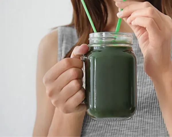 Une femme boit un smoothie vert à la spiruline, un allié pour la santé et la beauté des cheveux.