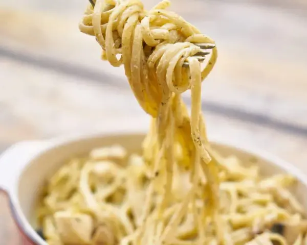 Une fourchette soulève des pâtes crémeuses, peut-être des pâtes cacahuète, d'un plat.