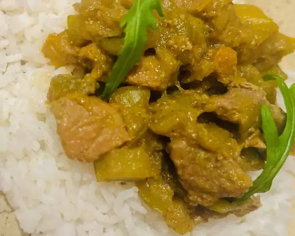 Un plat de riz blanc garni d'un curry vert aux légumes et morceaux de viande.