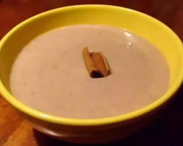 Un bol jaune contient une crème onctueuse de banane au lait de coco, garnie d'un bâton de cannelle.