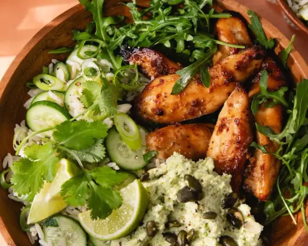 Un bol de riz au miso avec poulet glacé, concombre, coriandre, roquette et une purée verte parsemée de graines.
