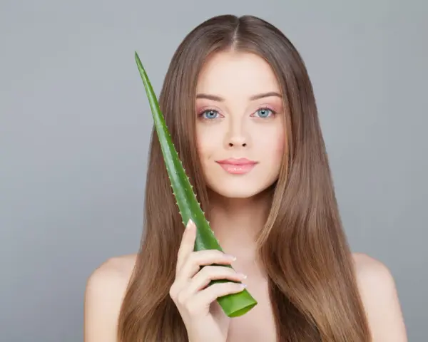 Une jeune femme aux cheveux longs tient une feuille d'aloe vera, montrant comment utiliser l'aloe vera pour une peau éclatante.