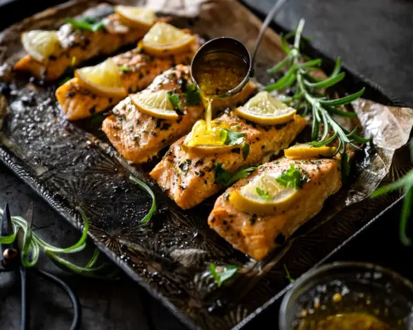 Filets de saumon sauce soja sucrée, garnis de citron et de persil, sur un plateau orné. Une louche verse la sauce.