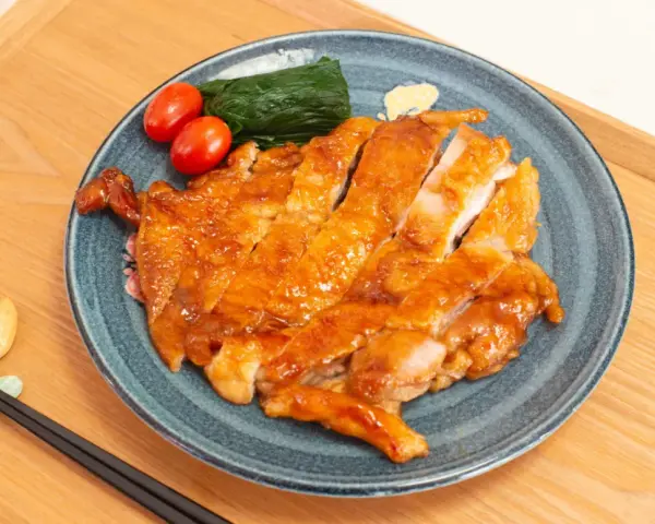 Délicieux poulet teriyaki recette, tranché et glacé, servi avec des tomates cerises et des épinards sur une assiette bleue.