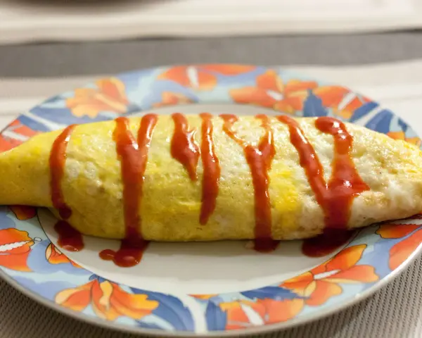 Une omelette japonaise au riz, nappée de ketchup, sur une assiette décorée de fleurs.