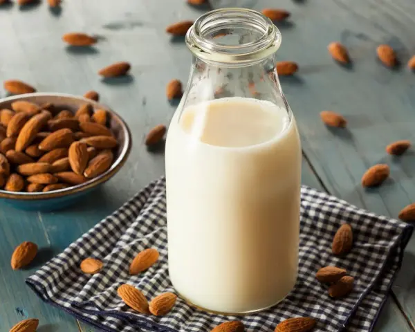 Bouteille de lait végétal d'amande, avec un bol d'amandes et des amandes éparpillées sur une table en bois bleu.