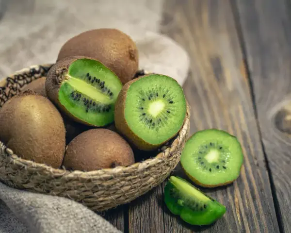 Un panier de kiwis frais, certains entiers, d'autres coupés, révélant leur chair verte et leurs pépins noirs. Attention, le kiwi peut provoquer une allergie.