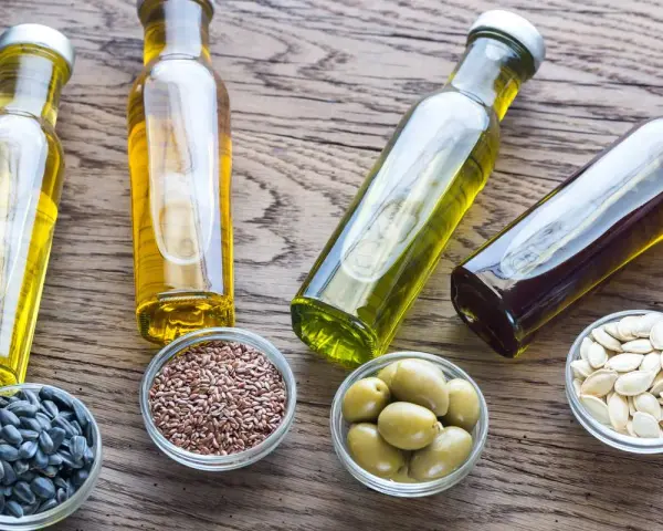 Bouteilles d'huile de cuisson dorée et ambrée, avec des graines de tournesol, de lin, des olives et des pépins de courge.