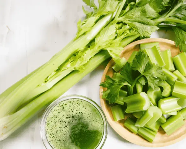 Jus de céleri frais, coupé en morceaux dans un bol en bois. Une branche entière de céleri est à côté. Attention à l'allergie céleri.