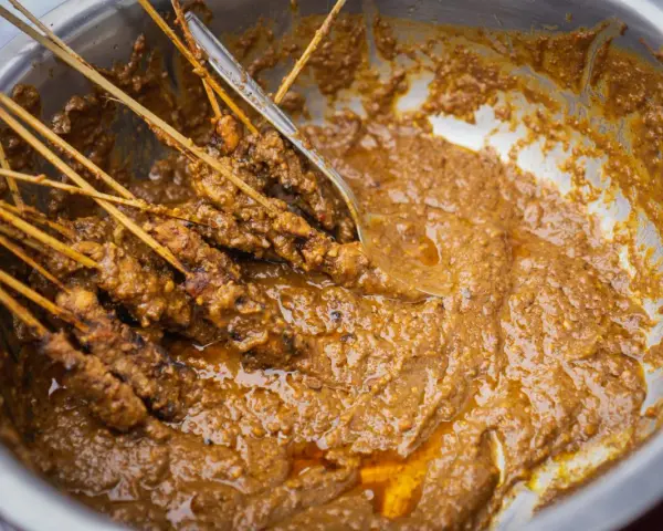Brochettes de poulet baignant dans une généreuse sauce satay crémeuse, prêtes à être dégustées.