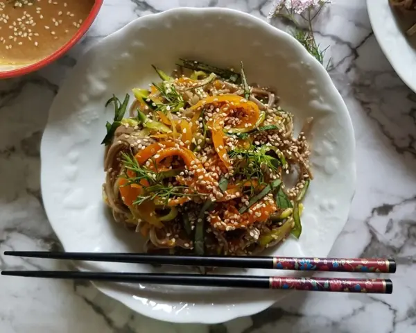 Salade de nouilles soba colorée avec des carottes, des courgettes et des graines de sésame, servie avec une sauce crémeuse.
