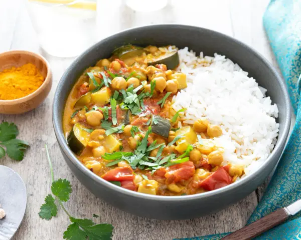 Un délicieux curry végétarien aux pois chiches, courgettes et tomates, servi avec du riz blanc et garni de coriandre fraîche.
