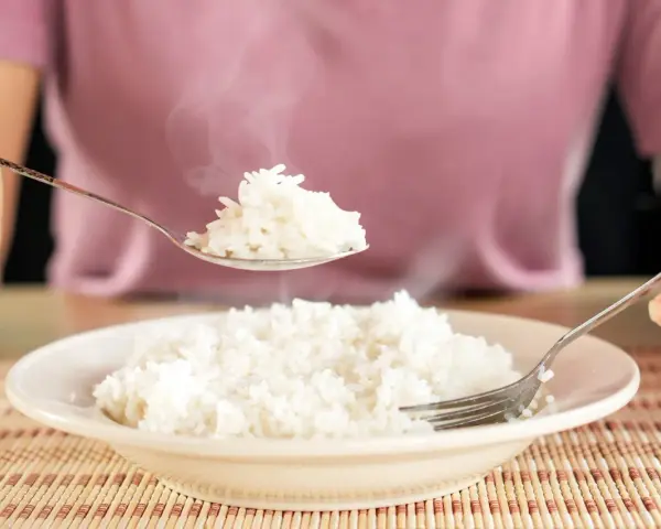 Une cuillère de riz blanc fumant, résultat d'une cuisson parfaite, est soulevée au-dessus d'une assiette remplie.