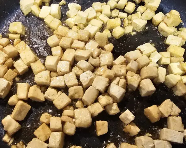 Dés cubes de tofu caramélisé dorent dans une poêle, prêts à être dégustés.