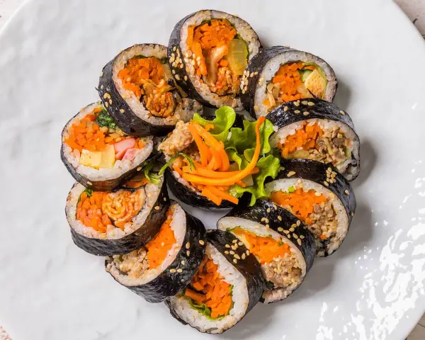 Un assortiment de makis végétariens colorés, garnis de carottes râpées, d'omelette et de légumes croquants, disposés en cercle sur une assiette blanche.