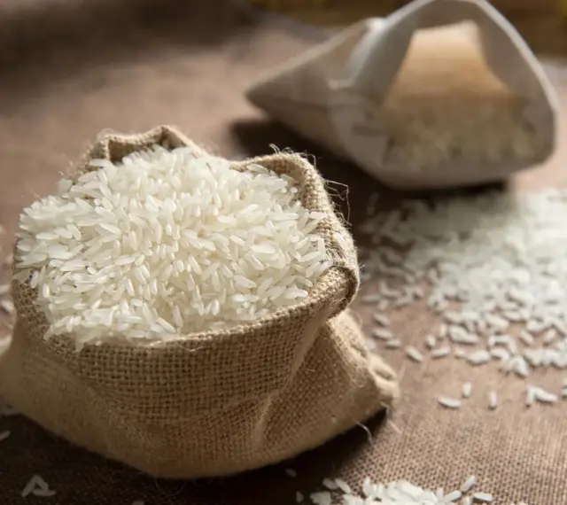 Un sac en toile de jute déborde de riz blanc, une céréale essentielle. Une autre bourse de riz est visible en arrière-plan.