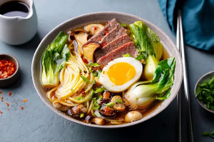 Un bol de pâte ramen savoureux avec des tranches de bœuf, un œuf mollet, des champignons et du bok choy.