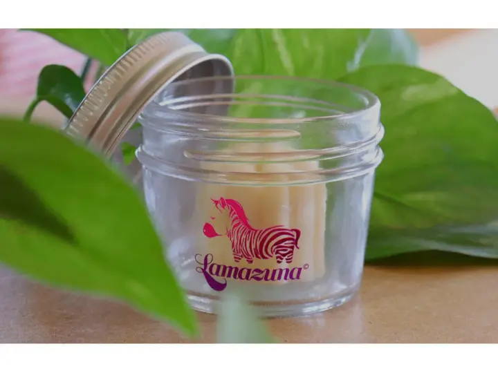 Petit pot en verre ouvert, révélant un baume solide. Le logo Lamazuna, un zèbre rose, orne le verre. Un soin naturel à base de beurre de cacao.