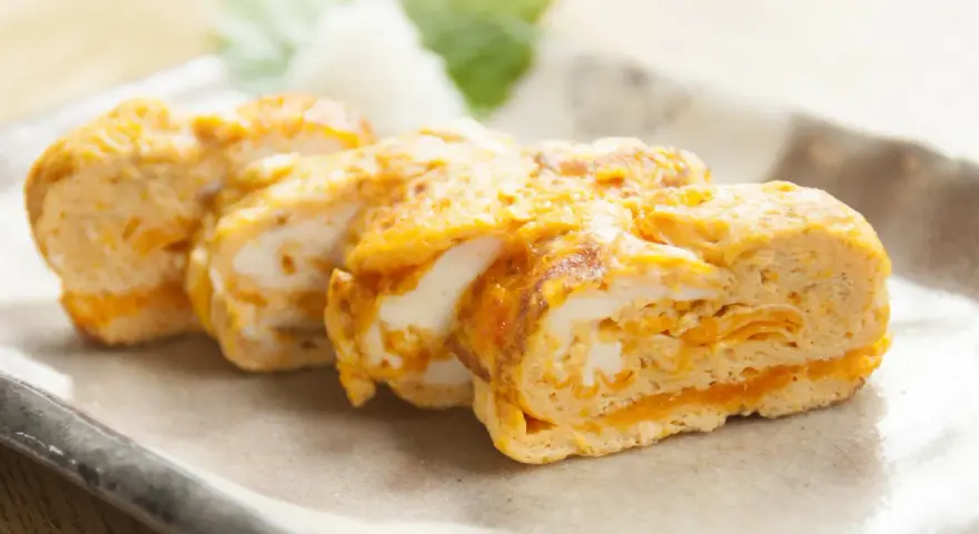 Délicieux oeuf japonais roulé, aux couches dorées et blanches, servi sur une assiette avec une feuille verte.