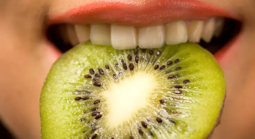 Une tranche de kiwi est mordue par des lèvres roses, ses petites graines noires contrastant avec la chair verte. Une sensation de kiwi langue qui pique.