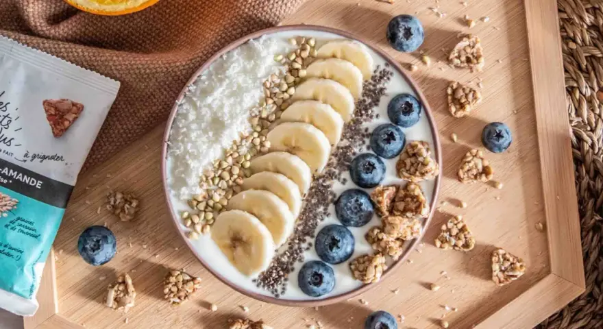 Un bol de smoothie aux bananes, myrtilles, noix de coco râpée et graines de chia, parfait pour un déjeuner au bureau sain et gourmand.
