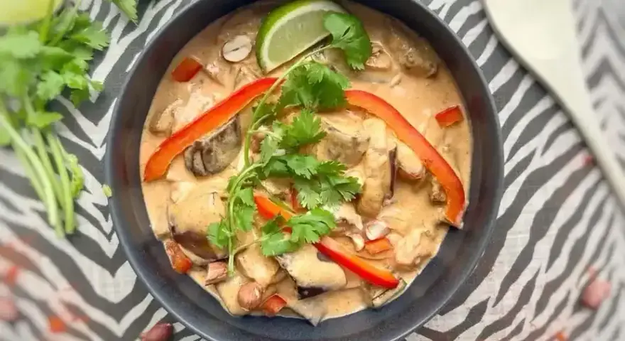 Un délicieux curry rouge, une composition appétissante avec des poivrons, de la coriandre et un quartier de citron vert.