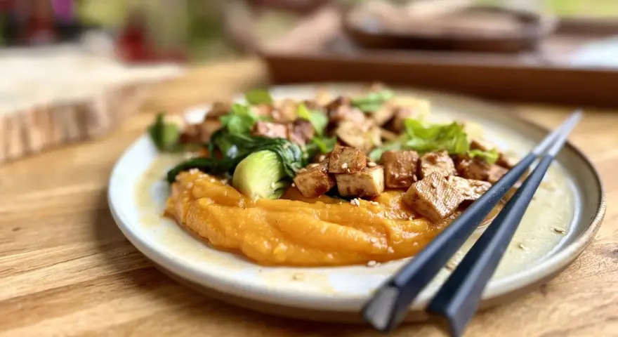Un plat savoureux de tofu miso sur une purée de patates douces, garni de légumes verts et de graines de sésame.